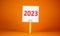 2023 happy new year symbol. Wooden clothespin, white sheet of paper with number 2023. Beautiful orange table orange background,