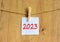 2023 happy new year symbol. Wooden clothespin, white sheet of paper with number 2023. Beautiful wooden background, copy space.