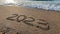 2023 numbers on the sandy beach, handwritten in the sand closeup. Slow motion. The wave washes away the inscription 2023