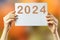 2024, Woman holding cardboard with number 2024 on orange background. Happy New Year