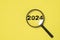 2024 year inside of magnifier glass on yellow background for focus and preparation new year change and start new business target