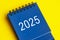 2025 blue desk calendar on yellow cover background.