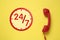 24/7 hotline service. Red handset on yellow background, top view