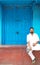 3 August, 2019 at Lucknow, Uttar Pradesh: Man in white kurta sitting on a porch with blue walls and door in the background.