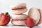 3 cookies with strawberry, beige French macaroons  with  pink cream on a white wooden background