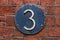 3 Digit on Dark Metal Background on red brick wall.