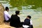 3 Jewish Hasidic boys in traditional clothes sitting near the lake in the park in Uman