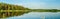 3 persons on the lonely boat in the middle of the lake that reflects forrest, under blue sky with clouds, panoramic background