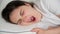 A 30-year-old brunette woman yawns lying on a pillow on her bed.