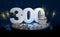 300th birthday or anniversary cupcake with big white number with yellow streamers on blue table with dark background full of