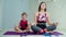 30s mother in sportswear doing meditation practice with young boy on fitness mat at home. Happy family meditate together