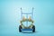 3d close-up rendering of big golden crown on blue hand truck on light-blue background.