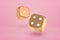 3d close-up rendering of two glossy gold dice bouncing on yogurt pink background.