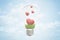 3d closeup rendering of lightbulb and green grass and four cute red hearts inside it, against blue sky with clouds.