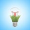 3d closeup rendering of lightbulb with white gift box tied with red ribbon on green grass inside bulb on light-blue