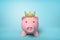 3d front close-up rendering of pink piggy bank wearing gold crown on light-blue background.