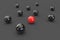 3D image of one red ball, among many black balls on a gray surface
