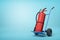 3d rendering of big red fire extinguisher on blue hand truck that is standing in half-turn on light-blue background with