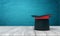 3d rendering of black tophat with red ribbon standing on wooden table near blue wall with copy space.