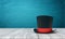 3d rendering of black tophat with red ribbon standing on wooden table near blue wall with copy space.
