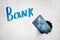 3d rendering of blue bank card breaking white wall with `Bank` sign on the background