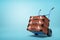 3d rendering of blue hand truck with stack of three brown suitcases on top on light-blue background with copy space.