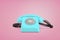 3d rendering of a blue retro rotary phone with a receiver on a cord stands on a pink background.
