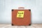 3d rendering of brown retro suitcase with yellow Vacation sign on wooden floor and white wall background.