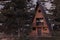 3d rendering of A-frame wooden cabin in forest full with pine trees in the evening light