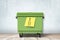 3d rendering of green trash can standing on wooden floor, yellow post-it note with hand-drawn bottle stuck onto can.