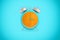 3d rendering of a large blue retro alarm clock with an orange peel instead of its face standing on a blue background.