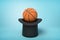 3d rendering of orange basketball ball on black top hat upside down on blue background