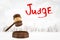 3d rendering of round wooden block and brown wooden gavel with red `Judge` sign on white city skyscrapers background