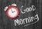 3d rendering of a top view on a red retro alarm clock lying on a wooden background near a white writing Good Morning.