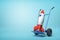 3d rendering of toy space rocket on blue hand truck which is standing in half-turn on light-blue background with copy