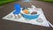 3D street anamorphic painting on asphalt in a park. View of blue chair near deep plate with toy hause and bird figure.