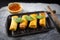4 fried spring rolls in a black ceramic plate and wooden chopsticks placed on a stone plate. Close up shot