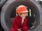 4 year old cute inquisitive boy in orange construction helmet and red work overalls sits on a construction site