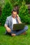 40s businessman sits with crossed legs on grass with laptop and mobile phone