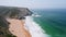 4K Aerial view of Praia da Adraga beach. White atlantic ocean waves rolling towards sandy beach with resting tourists