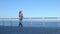 4K Beautiful woman walking down pier. The blue calm sea in on the side