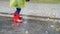 4k closeup slow motion video of child wearing red rubber wellington boots and raincoat jumping and walking in big puddle