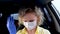 4k Curly blonde girl driver putting on medical mask and protective gloves in car before driving. Woman in yellow summer