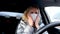 4k Curly blonde girl driver putting on two medical mask and blue protective gloves in car before driving. Woman in warm