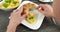 4K: Cut open croissant and some scrambled eggs lie on an angular white plate. A woman is putting some fresh scrambled eggs to the