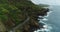 4K Drone Coastal Roadway Rocky Shore Crashing Waves Mountainside Flying Backwards
