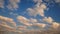 4K footage of white puffy with orange color of clouds float across a summer blue sky at sunset or sunrise time, camera pan motion