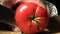 4k. Hands cut off red tomato on a wooden Board in the kitchen.