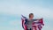 4k. Happy little boy spinning with USA flag outdoors over blue sky at summer - waving american flag, country, patriotism