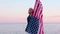 4k. happy smiling woman in summer clothes with national USA flag outdoors ocean sunset - American flag, country